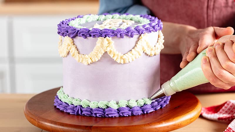 a person adding frosting decorations to a cake on a cake wheel with different shades of purple