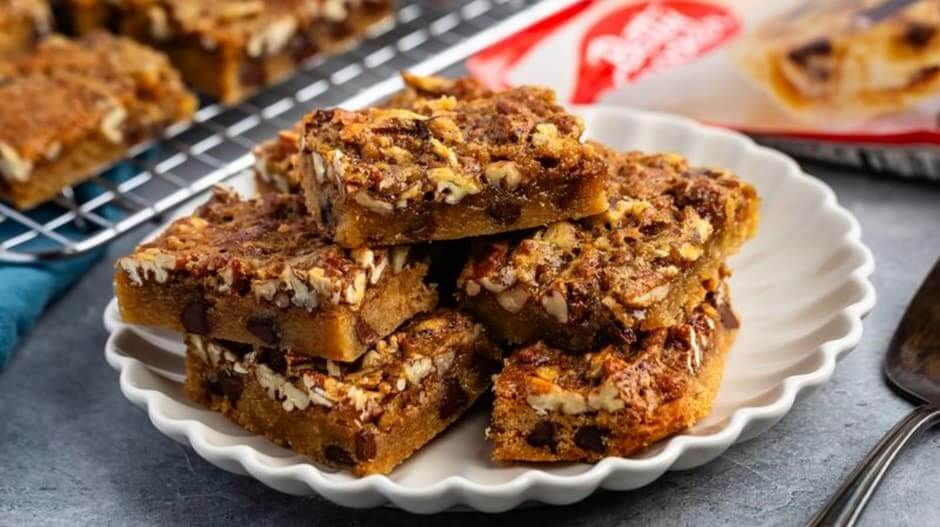 A plate of freshly baked pecan brownies beside a Betty Crocker mix box, cooling on a wire rack with a spatula nearby on a kitchen counter.